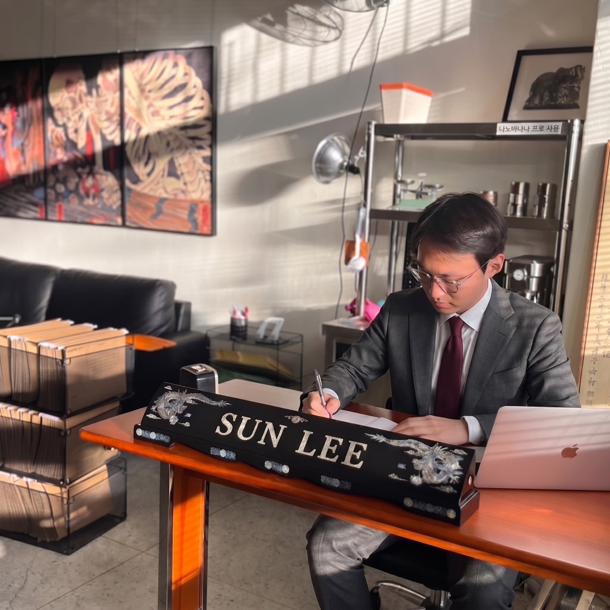 Sun Lee writing a Korean saju reading by hand at his Seoul desk, nameplate in front